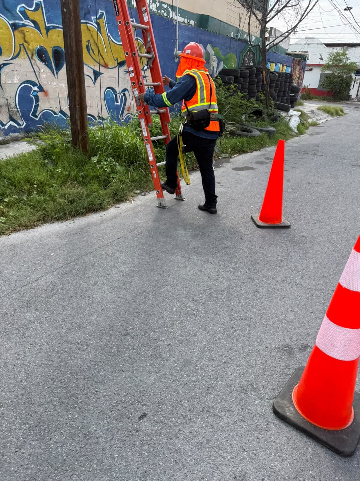 Técnico con equipo de seguridad preparando una escalera junto a un poste de telecomunicaciones