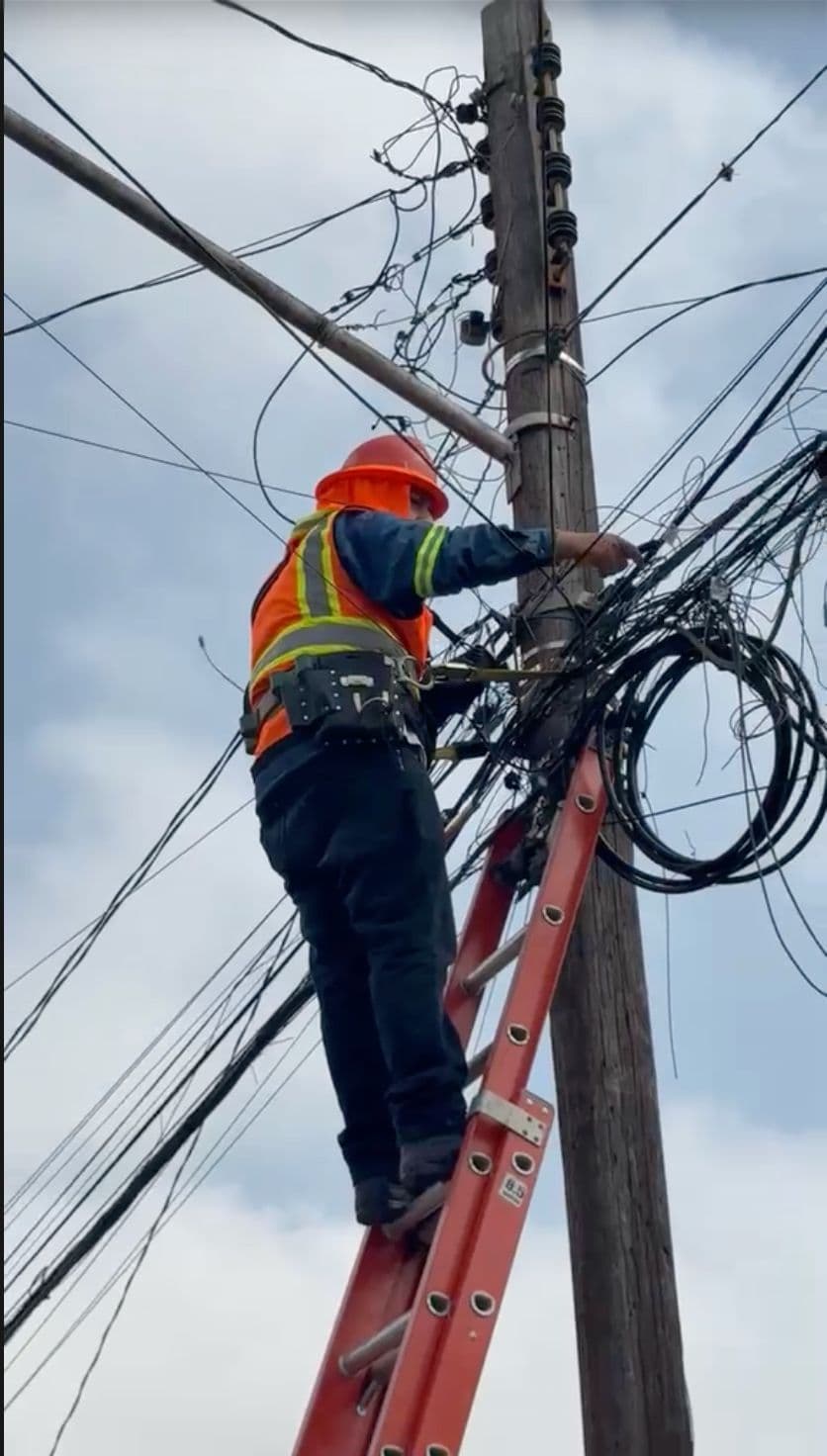 Técnico instalando cableado de fibra óptica desde una escalera junto a un poste